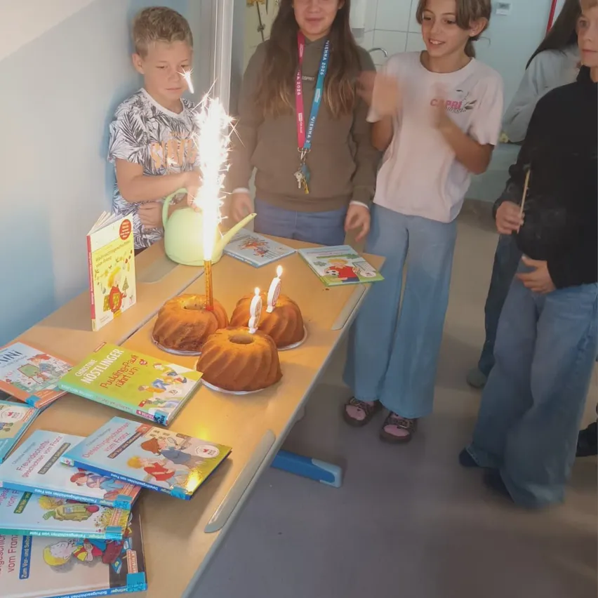 Eine Gruppe von Kindern feiert einen Geburtstag mit Kuchen und Büchern auf einem Tisch.