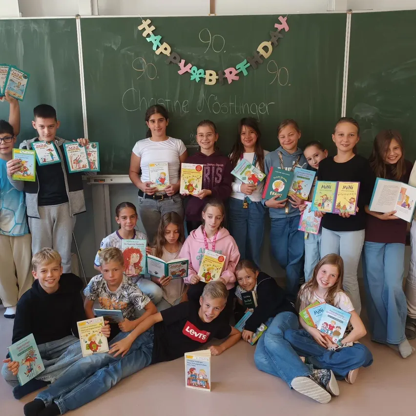 Eine Gruppe von Kindern und Erwachsenen posiert für ein Foto im Klassenzimmer. Sie halten Bücher und lächeln.
