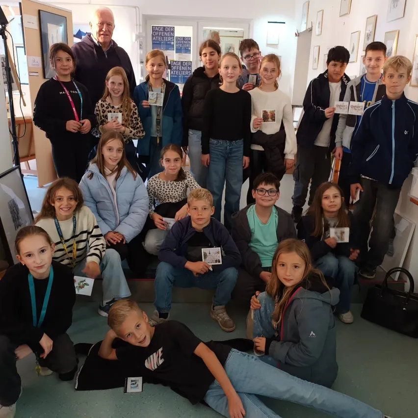 Eine Gruppe von Kindern und Erwachsenen posiert für ein Foto in einem Raum mit weißen Wänden und Bilderrahmen.