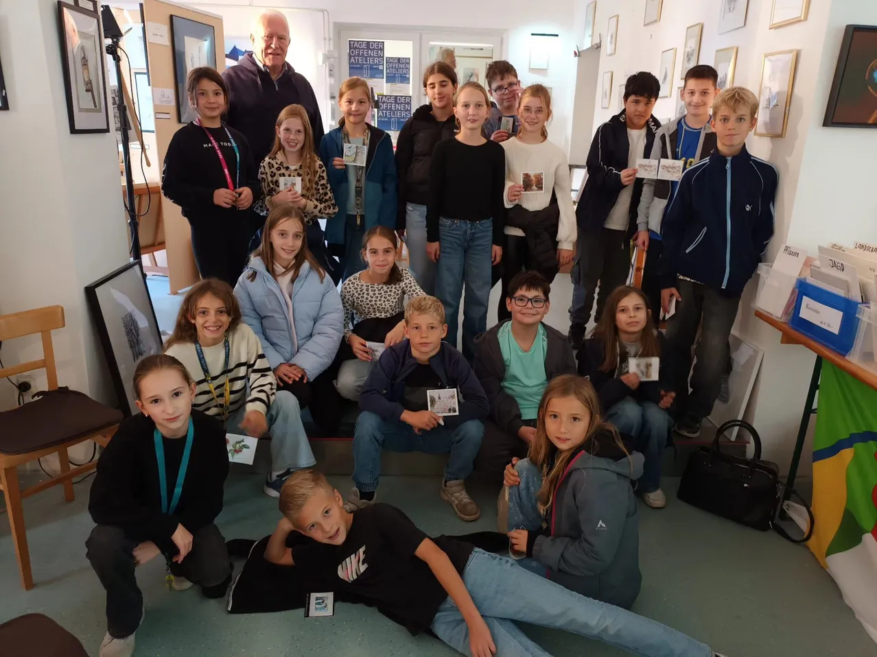 Eine Gruppe von Kindern und Erwachsenen posiert für ein Foto in einem Raum mit weißen Wänden und Bilderrahmen.