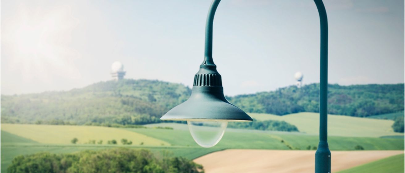 Eine Straßenlampe befindet sich auf einem grünen Feld mit Blick auf einen Hügel und zwei weiße Kuppeln in der Ferne.