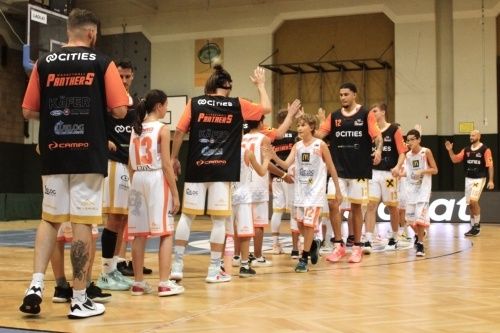 Eine Basketballmannschaft feiert einen Sieg auf dem Spielfeld, mit Spielern und Trainern in orange-schwarzen Trikots mit dem Logo Cities Panthers 5.