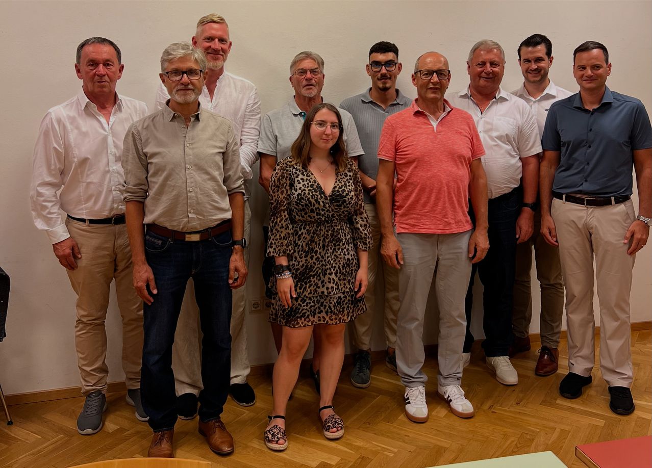 Eine Gruppe von Personen, darunter Männer und Frauen, posiert für ein Foto in einem Raum mit Holzboden.