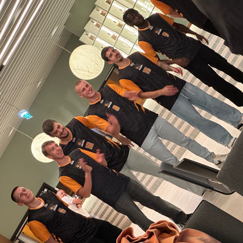 Fünf Männer in gleichen Trikots stehen in einer Bowling-Halle. Die Männer lächeln und posieren für ein Foto.