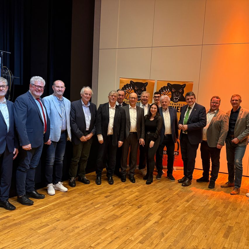 Eine Gruppe formell gekleideter Personen, einschließlich Männer und Frauen, posiert für ein Foto vor Bannern mit einem schwarzen Panther-Logo.