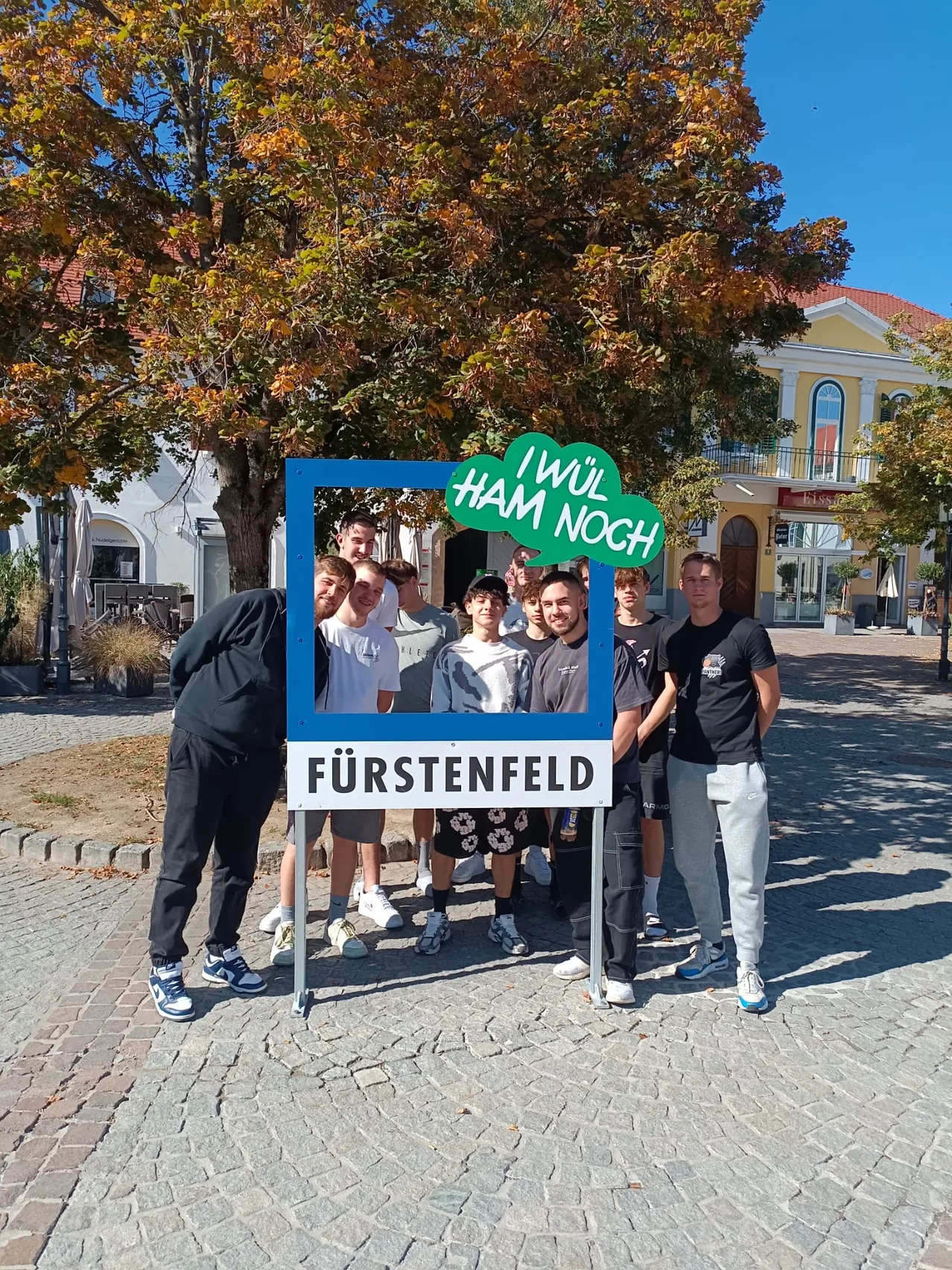Eine Gruppe von Menschen steht vor einem Schild mit der Aufschrift 'Fürstenfeld'.