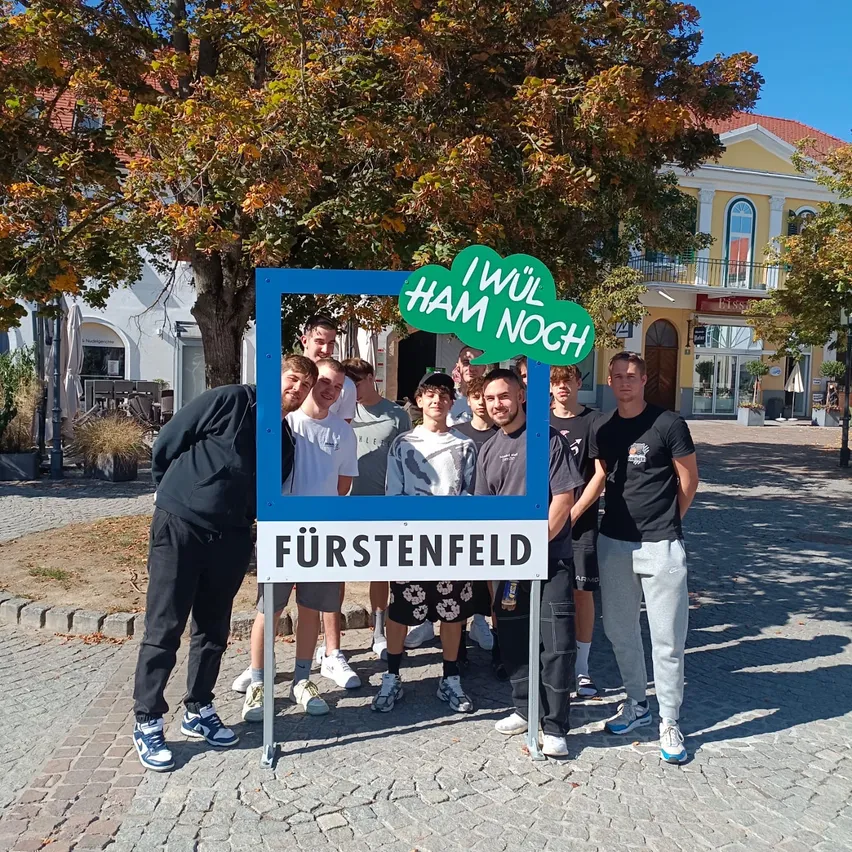 Eine Gruppe von Menschen steht vor einem Schild mit der Aufschrift 'Fürstenfeld'.
