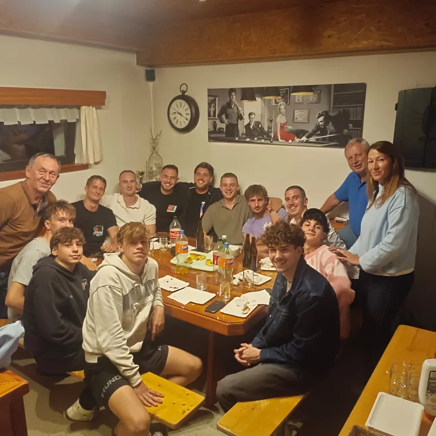 Eine Gruppe von Menschen sitzt um einen Esstisch in einem Raum und lächelt für ein Foto.