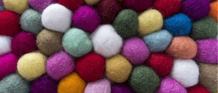 A vibrant collection of felt balls in various colors such as red, yellow, green, blue, white, and orange. They are arranged closely together, possibly used for decorative purposes.
