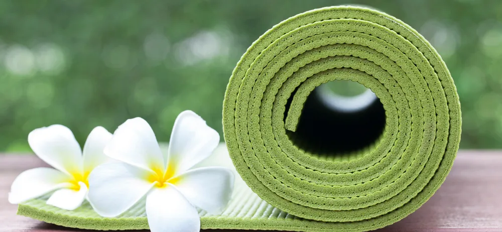 Eine aufgerollte grüne Yogamatte mit weißen Plumeria-Blumen auf einem Holztisch.