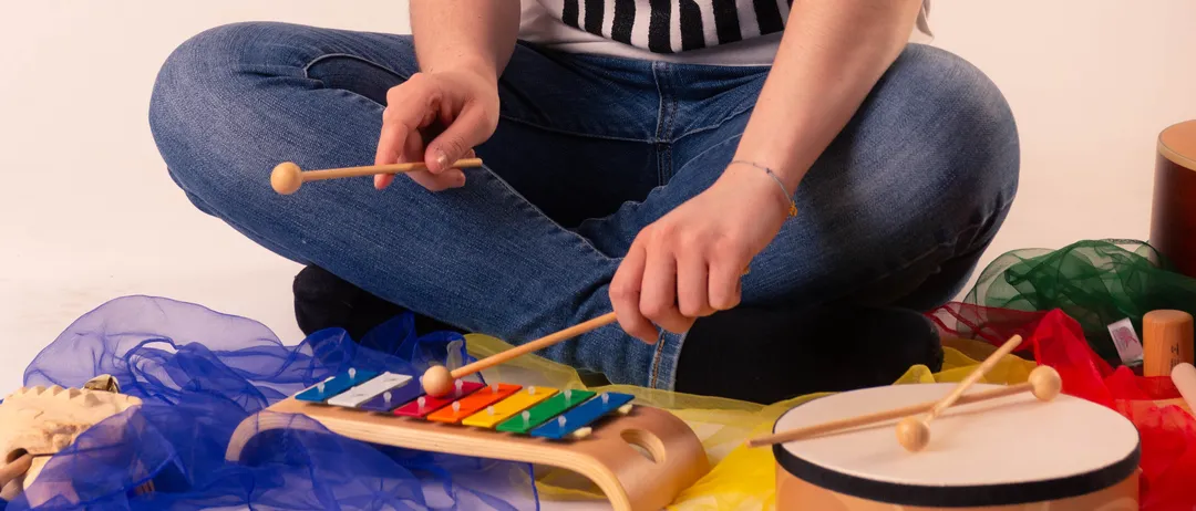 Eine Frau sitzt auf dem Boden und spielt ein Xylophon mit einem Trommel und anderen Musikinstrumenten um sie herum.