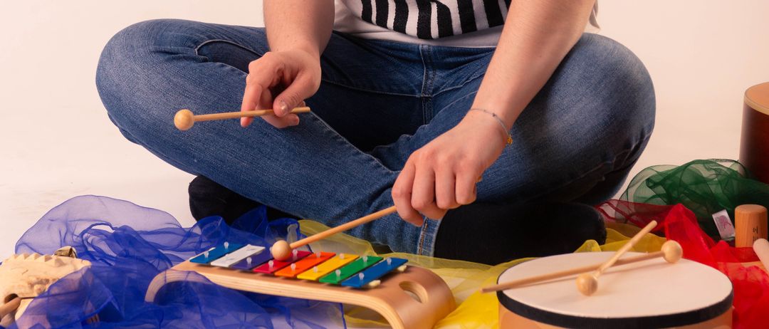 Eine Frau sitzt auf dem Boden und spielt ein Xylophon und eine Trommel mit einem Stock.