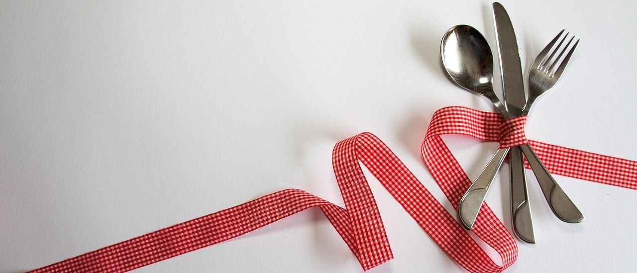 Ein Nahaufnahme von Besteck—ein Messer, Löffel und Gabel—mit einem roten Band auf einem weißen Hintergrund gebunden.