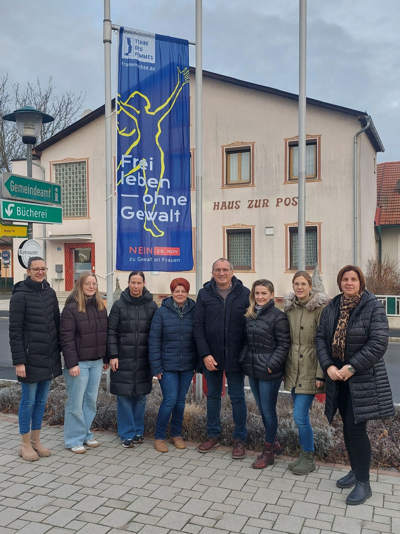 Eine Gruppe von Frauen und Männern steht vor einem Gebäude mit einem Banner, das Frei leben ohne Gewalt steht. Sie sind in Winterkleidung gekleidet und scheinen für ein Foto zu posieren.