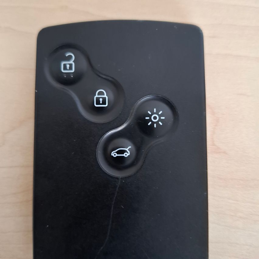 Schwarze Autofernbedienung mit vier Tasten. Oben links ist ein aufgeschlossenes Vorhängeschloss, oben rechts ein verschlossenes Vorhängeschloss. Unten links ein Auto-Symbol und unten rechts ein Lichtsymbol.