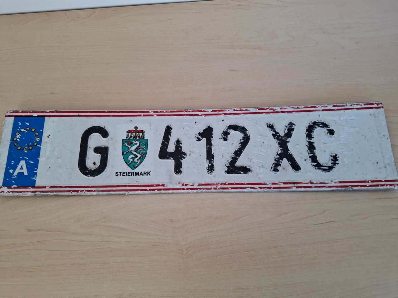 Ein altes österreichisches Nummernschild aus der Steiermark-Region, mit der Nummer G412XC, auf einer Holzoberfläche liegend.