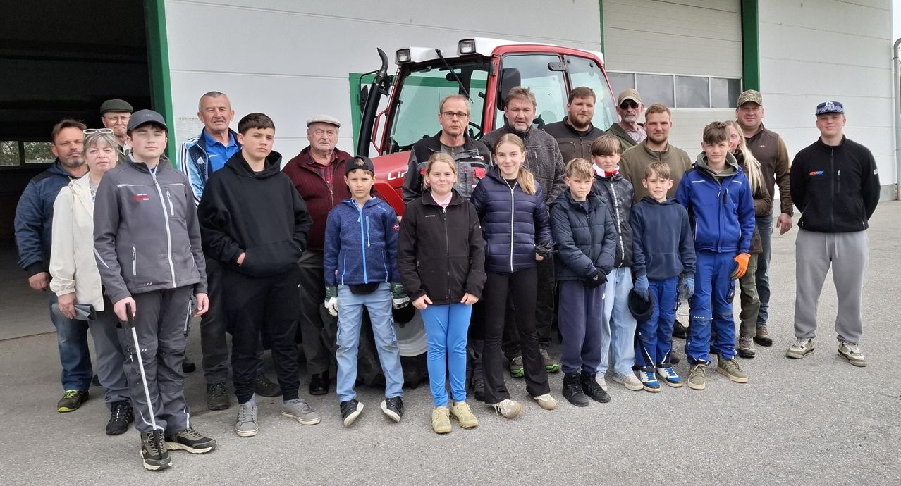 Eine Gruppe von Menschen steht vor einem roten Traktor. Erwachsene und Kinder tragen alle Jacken. Einige tragen Handschuhe. Sie posieren für ein Foto.