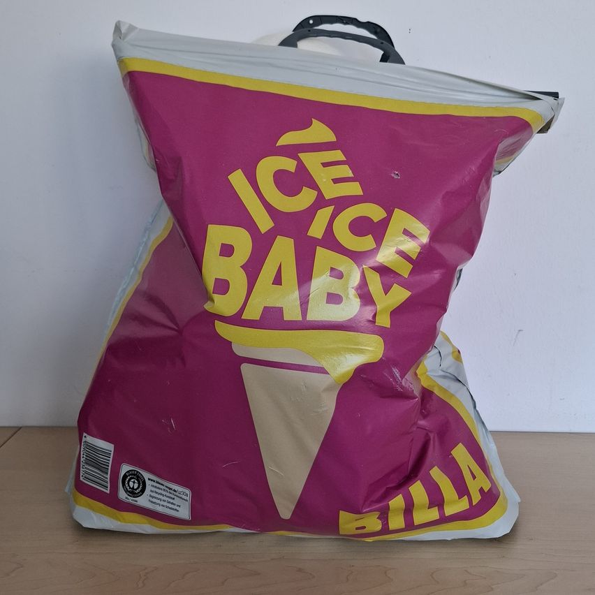 Ein rosa und weißer Beutel mit 'ICE ICE BABY' und 'BILLA' darauf geschrieben. Der Beutel ist leicht zerrissen und scheint mit Eis gefüllt zu sein.