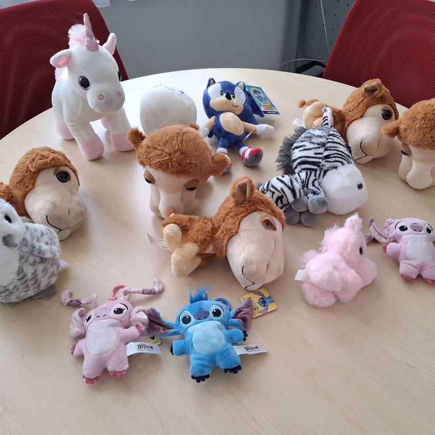 Eine Sammlung von Plüschtieren auf einem Holztisch, darunter Sonic, Einhörner, Zebras und andere Tiere.