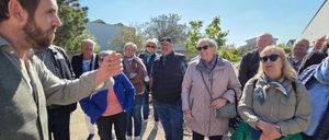 Eine Gruppe von Menschen steht zusammen im Freien, einige mit Sonnenbrille, an einem sonnigen Tag. Sie scheinen in ein Gespräch vertieft zu sein.