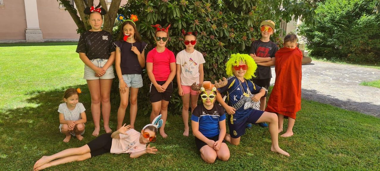 A group of children, all wearing various themed glasses, posing for a group photo in the garden. One child has a big yellow wig.