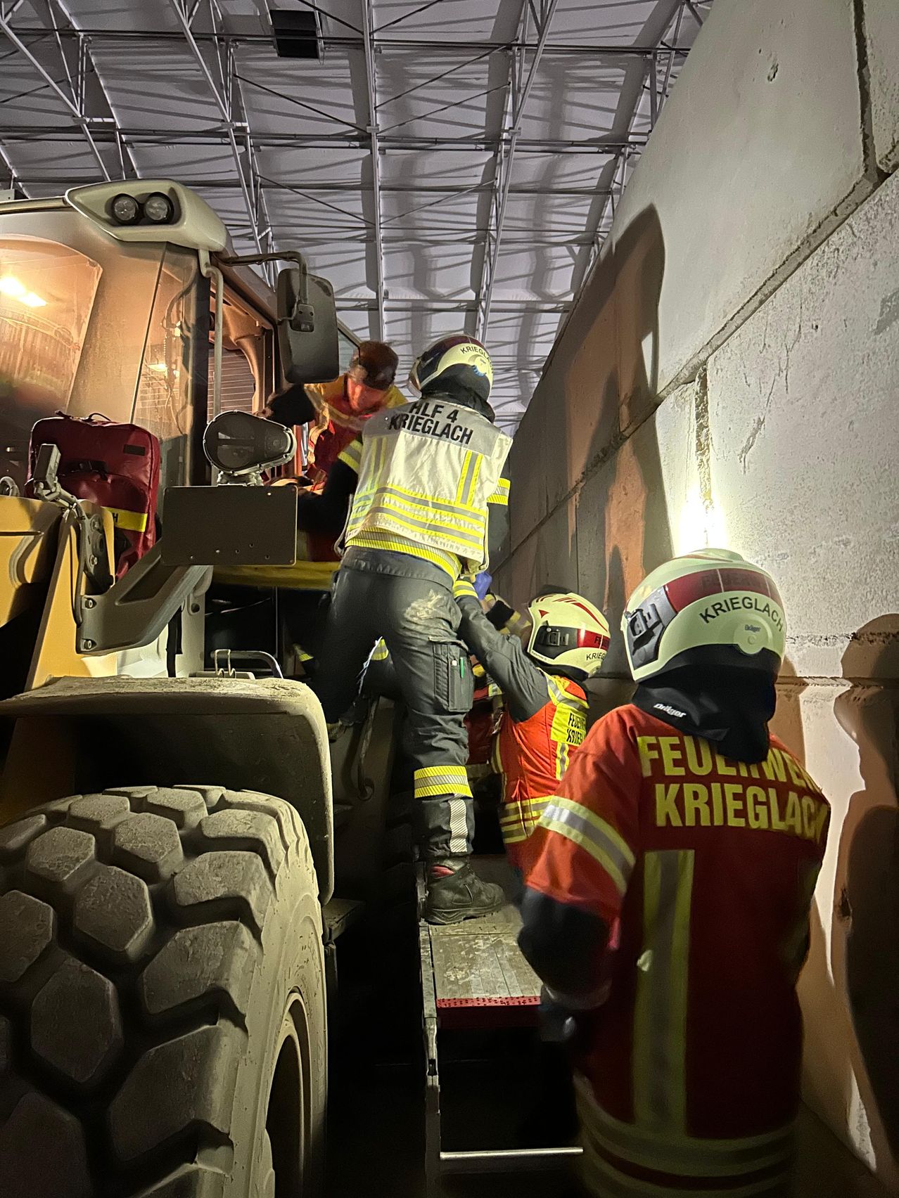 Three firefighters in safety gear are operating a heavy machinery vehicle. One is climbing into the driver's seat while others are holding the vehicle steady.