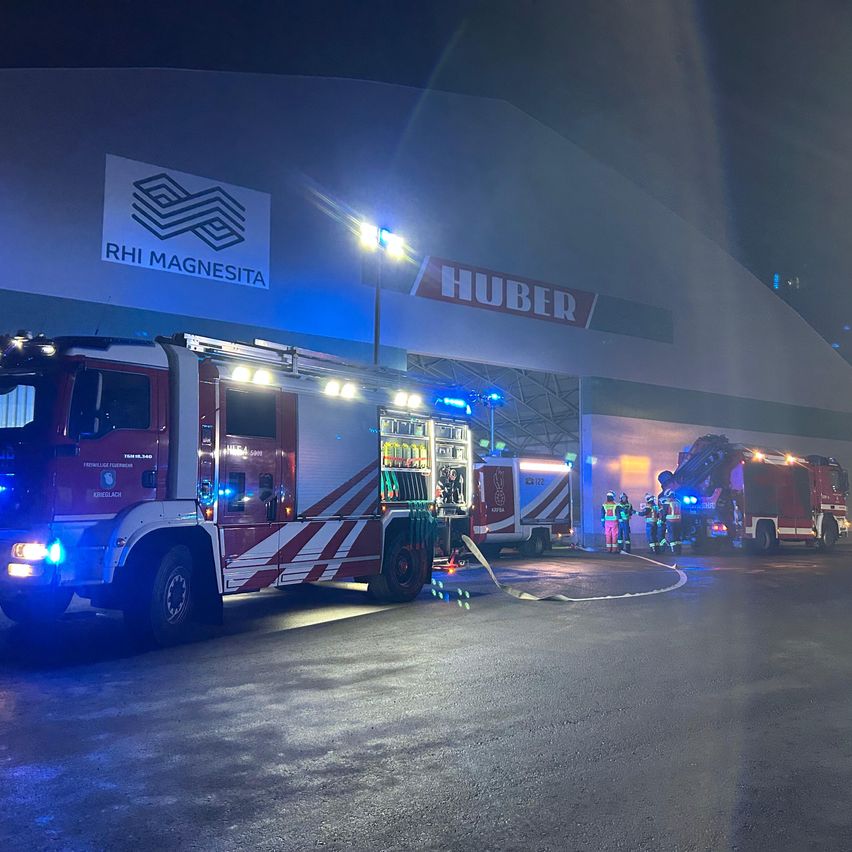 Two fire trucks are parked in front of a RHI Magnesita building, with firefighters attending to an incident.