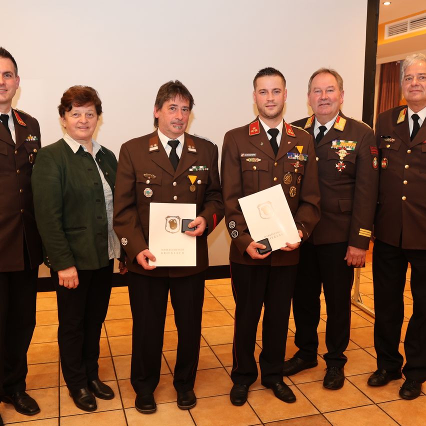 Eine Gruppe von Menschen in Militäruniformen, darunter eine Frau, steht zusammen und hält Urkunden in den Händen. Sie lächeln, und Medaillen und Abzeichen sind an ihren Uniformen sichtbar. Der Ort scheint eine formelle Veranstaltung zu sein.