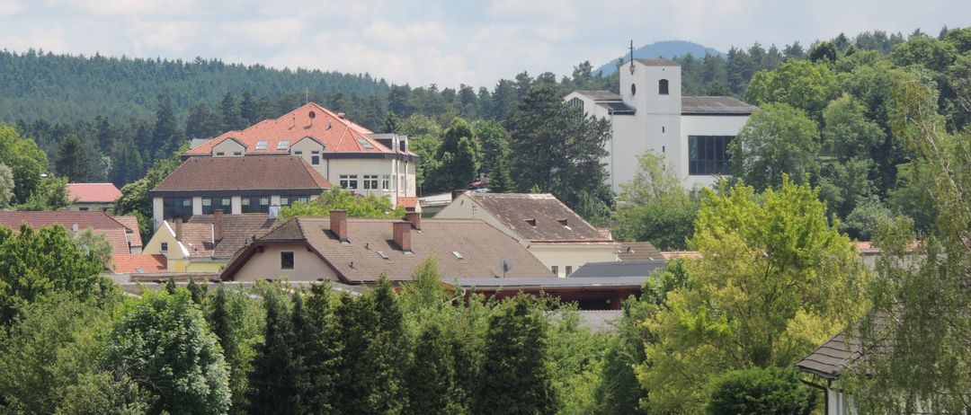 Eine malerische Luftaufnahme einer Stadt mit mehreren Gebäuden, umgeben von üppigem Grün und Bäumen unter einem teilweise bewölkten Himmel.