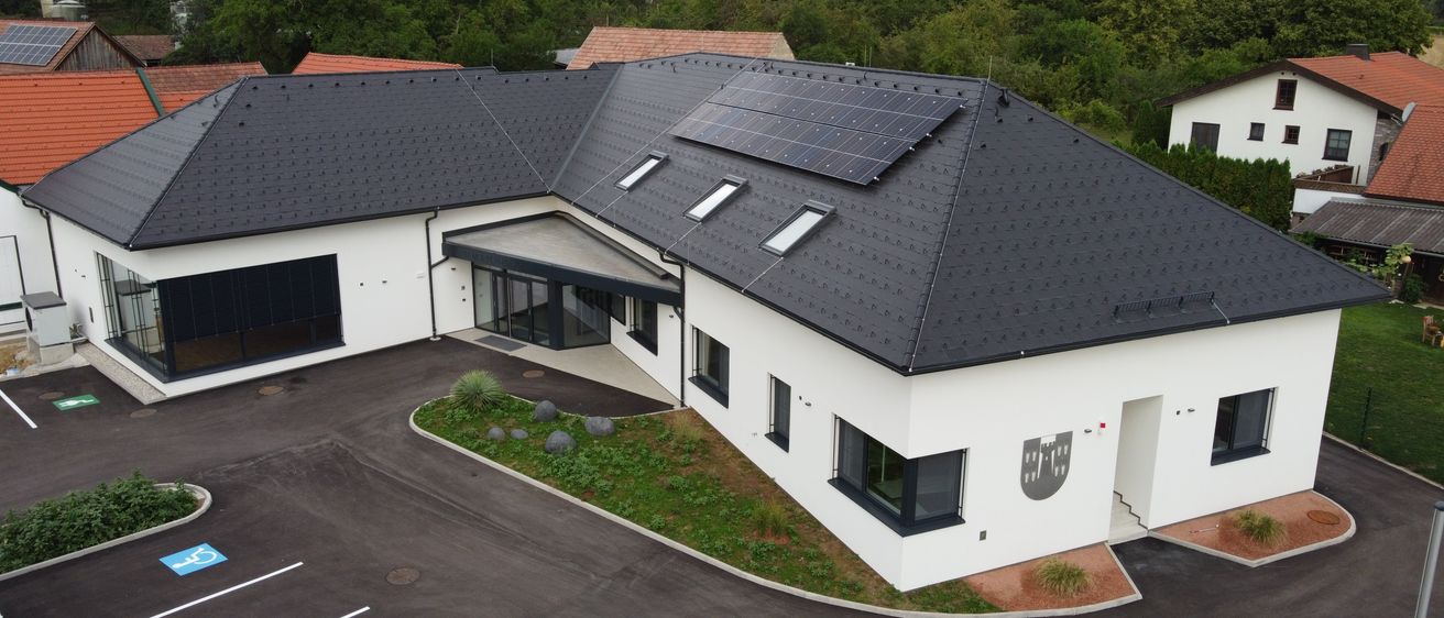 Luftaufnahme eines modernen Hauses mit Solarmodulen auf dem Dach, umgeben von Grün und Bäumen.
