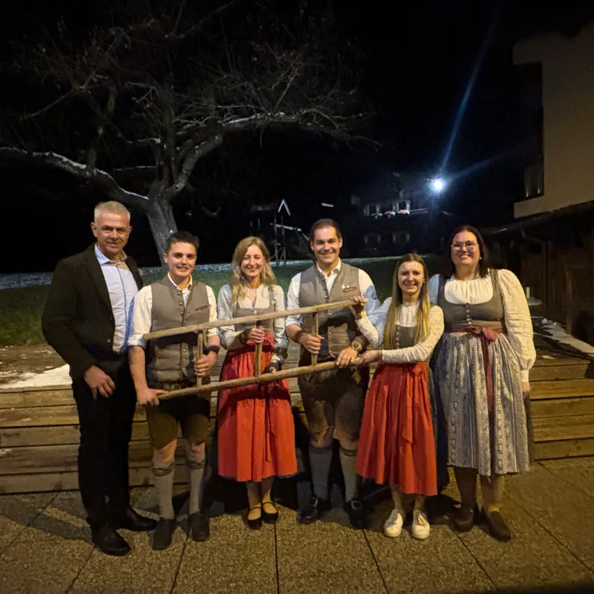 Eine Gruppe von Menschen posiert nachts für ein Foto. Sie tragen alle traditionelle Kleidung. Zwei von ihnen halten eine Holzleiter.