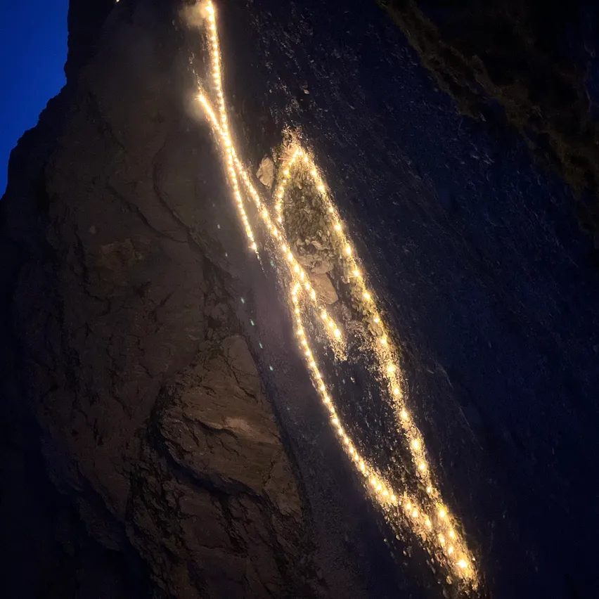 Ein Nachtblick auf einen Berg mit einer Reihe von Lichtern, die an seinem steilen Hang befestigt sind und einen Pfad beleuchten.