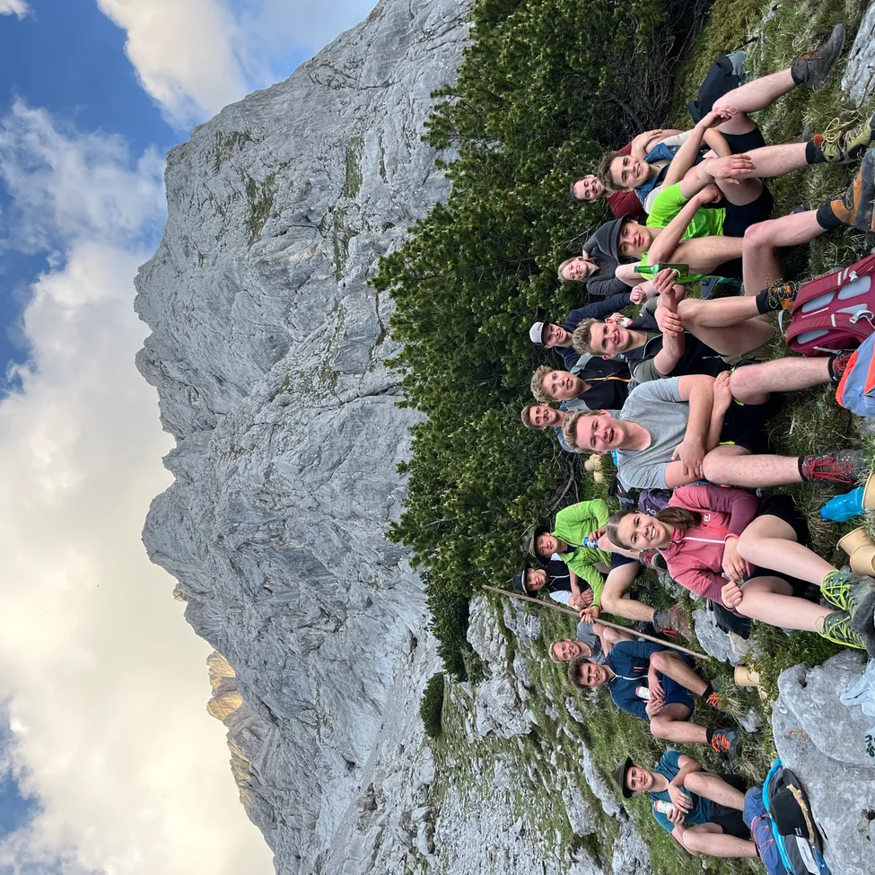 Eine Gruppe von Wanderern posiert für ein Foto auf einem Bergpfad, lächelnd und umgeben von Grün und Felsgelände.