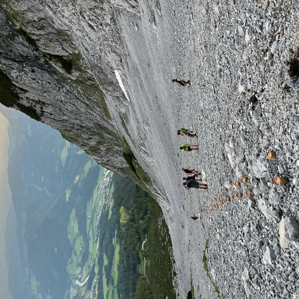 Eine Luftaufnahme von mehreren Wanderern, die auf einem felsigen Felsvorsprung gehen. Sie befinden sich auf einem Bergpfad.