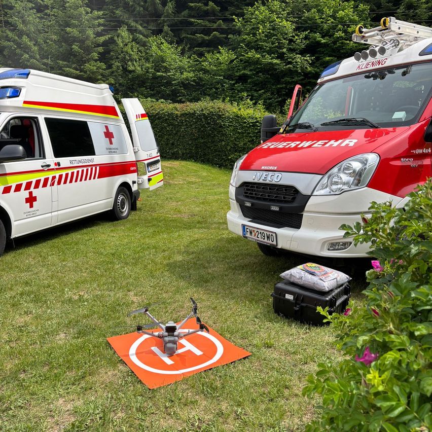Zwei Rettungswagen stehen auf einem Rasen, mit einem Drohnen davor. Ein Krankenwagen hat das Wort Rettungdienst an seiner Seite, und der andere sagt Feuerwehr.