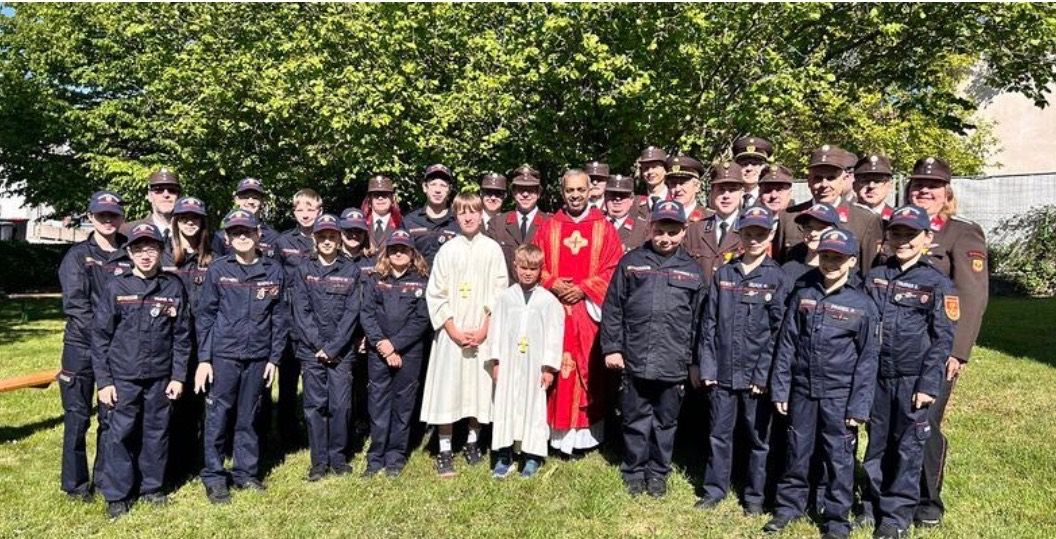 Eine Gruppe uniformierter Personen steht im Freien zusammen, einschließlich Kinder und Erwachsene, einige in Hüten und andere in religiöser Kleidung, posieren für ein Foto.