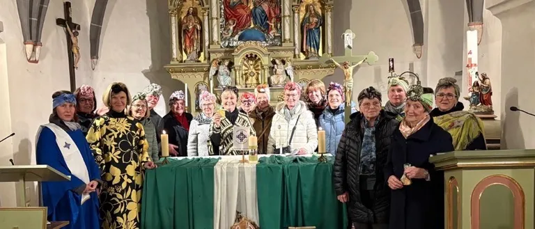 Eine Gruppe von Menschen versammelt sich in einer Kirche und steht vor einem Altar. Sie tragen Hüte und Gewänder. Der Altar ist mit Blumen, Kerzen und anderen Gegenständen geschmückt. Hinter ihnen befindet sich eine Wand mit einem Kruzifix und einer Statue. Das Bild hat einen Wasserzeichen mit dem Text 'STUFF'.