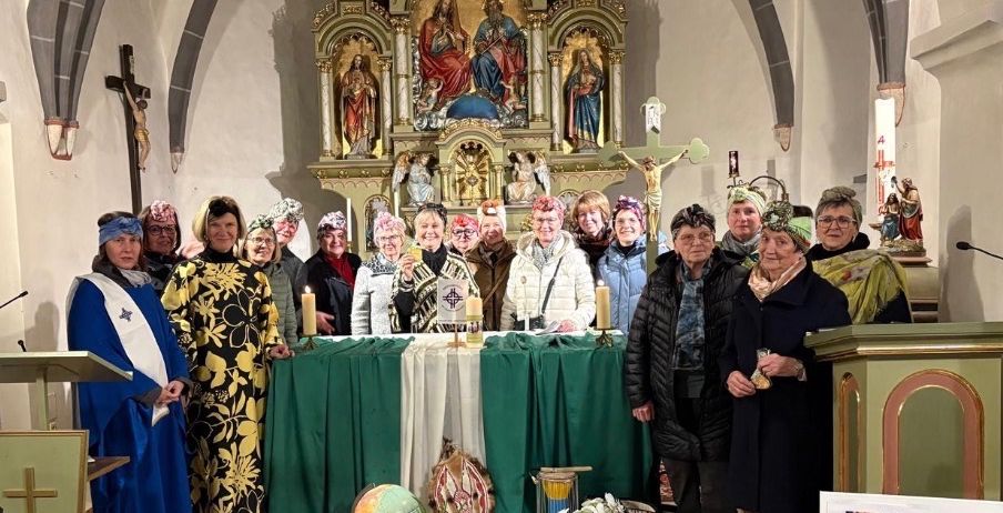 Eine Gruppe von Menschen versammelt sich in einer Kirche und steht vor einem Altar. Sie tragen Hüte und Gewänder. Der Altar ist mit Blumen, Kerzen und anderen Gegenständen geschmückt. Hinter ihnen befindet sich eine Wand mit einem Kruzifix und einer Statue. Das Bild hat einen Wasserzeichen mit dem Text 'STUFF'.