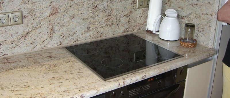 Eine Küche mit Granitarbeitsplatte verfügt über einen Herd mit Digitalanzeige, eine weiße Kaffeekanne und eine Rolle Küchenpapier. Es gibt Steckdosen an der Wand und ein Schrank mit einem Korb.