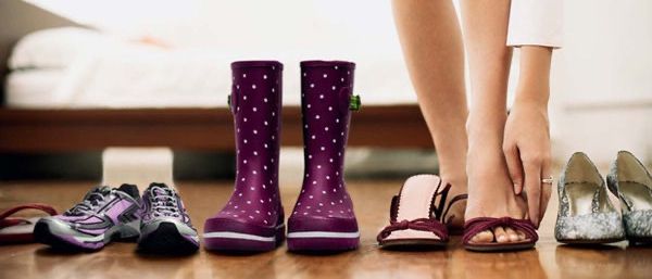 Eine Person im Schlafzimmer, mit gebeugtem Knie, hält einen Stiefel und steht neben Schuhen auf dem Boden.