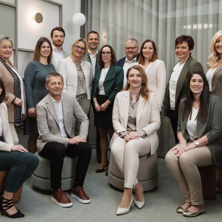 Eine Gruppe von Menschen in formeller Kleidung posiert für ein Foto. Sie stehen und sitzen in einem gut beleuchteten Raum.