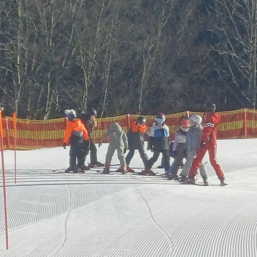Eine Gruppe von Menschen in Skiausrüstung steht auf einem verschneiten Hang. Sie befinden sich vor einer rot-gelben Barriere.