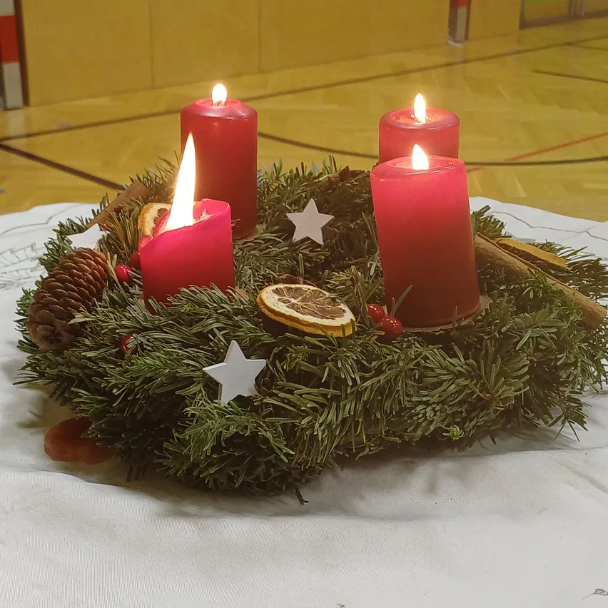 Ein Weihnachtskranz mit drei roten brennenden Kerzen und Tannenzapfen, Sternen und Zimtstangen auf einem weißen Tuch.
