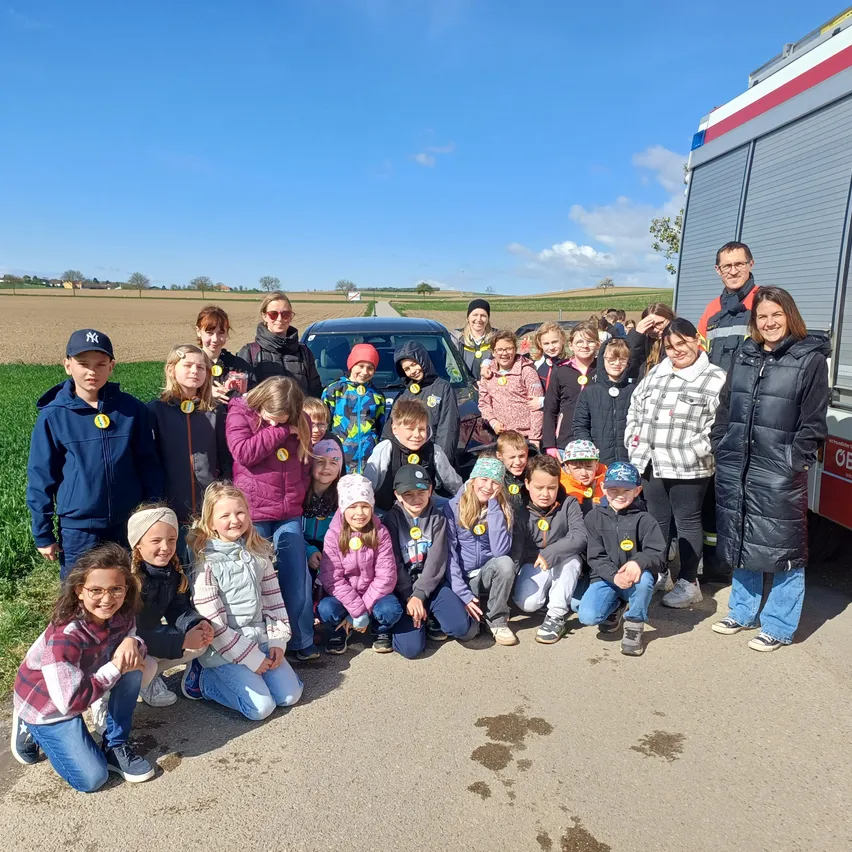 Eine Gruppe von Kindern und Erwachsenen posiert für ein Foto vor einem Feuerwehrauto auf einem Feld.