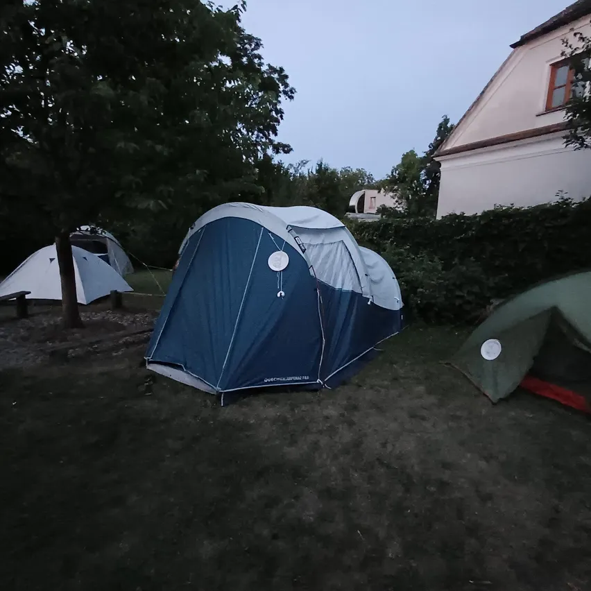 Drei Zelte stehen auf Gras in einem Campingbereich bei Nacht. Ein Zelt ist blau, ein weiteres grün und ein weißes im Hintergrund.