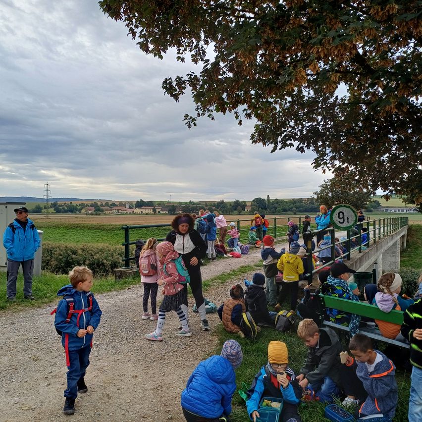 Schulklasse mit Betreuern und Kindern auf einem Feldweg bei einer Brücke mit 9t-Schild.