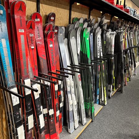Ein Geschäft mit einer Vielzahl von Skiern zur Schau, darunter rote, schwarze, blaue und weiße Skier an einer Holzwand.
