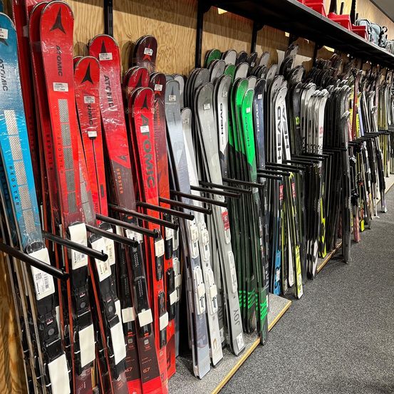Ein Geschäft mit einer Vielzahl von Skiern zur Schau, darunter rote, schwarze, blaue und weiße Skier an einer Holzwand.