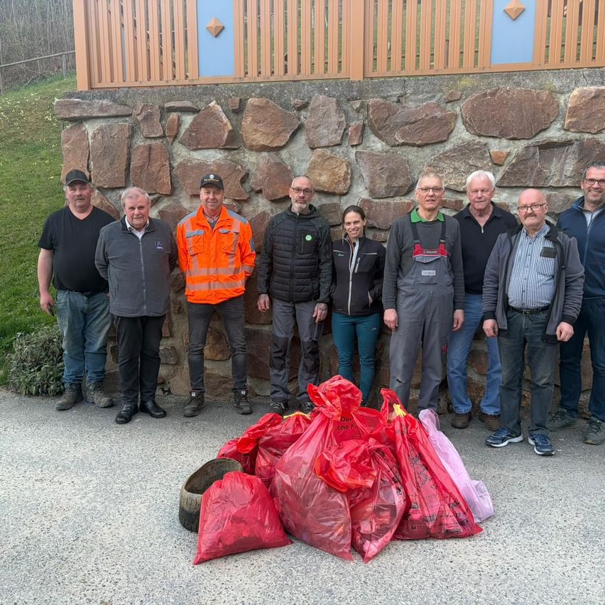 Gruppe von Männern, die hinter einer Steinmauer stehen, Jacken, Hosen und Schuhe tragen, mit Säcken voller Müll vor ihnen.