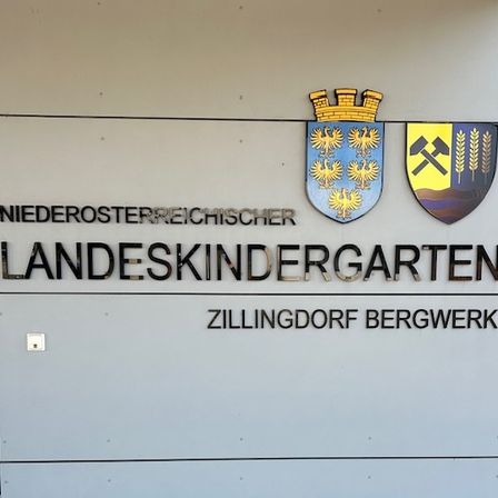 Ein Schild für Niederosterreichischer Landeskindergarten Zillingdorf Bergwerk, mit zwei Wappen über dem Text.